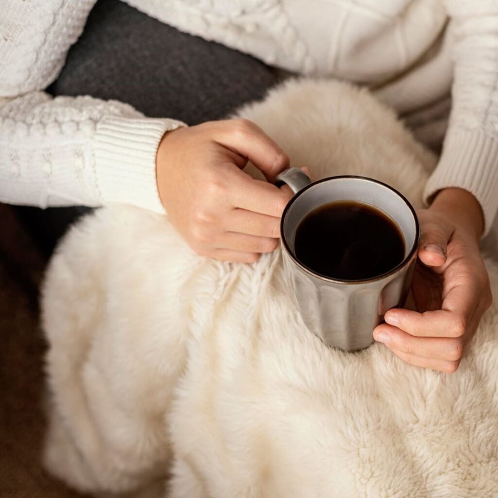 Mains tenant une tasse sous un plaid en fausse fourrure